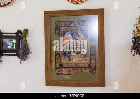 Icône folklorique encadrée verticalement avec des tons dorés et terreux sur un mur blanc flanqué d'herbes et d'assiettes capturant la chaleur d'une maison traditionnelle et le ch Banque D'Images