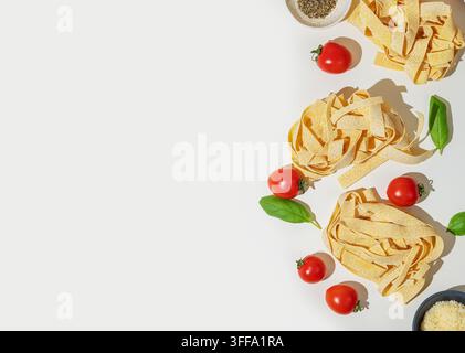 Nids de pâtes fraîches aux tagliatelles, tomates cerises, feuilles de basilic, fromage râpé et herbes séchées sur fond blanc. Concept de cuisine italienne. Vue de dessus Banque D'Images