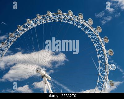 Vue en contre-plongée de la grande roue d'observation du London Eye avec des capsules passagers en verre sur un ciel bleu parsemé de nuages blancs lors d'une journée ensoleillée. Banque D'Images