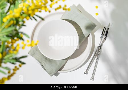 Décoration de table festiv pour la célébration printanière de la journée de la femme, d'un mariage ou de la fête des mères avec des fleurs de mimosa jaunes sur un fond clair baigné de lumière. Res Banque D'Images