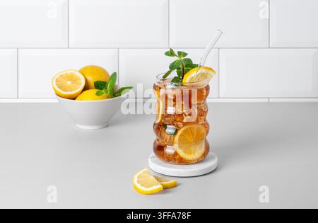 Thé glacé au citron, glace et menthe dans un verre sur le plan de travail de la cuisine avec des agrumes et un fond de mur en briques blanches. Concept tendance de rafraîchissement Banque D'Images