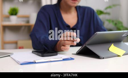 Gros plan d'une femme d'affaires asiatique tenant un stylet et travaillant sur une tablette numérique au bureau. Entrepreneure professionnelle analysant un rapport, document Banque D'Images