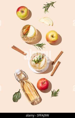 Flat lay de cocktail ou cidre de pomme dans un verre avec glace, cannelle et romarin, bouteille et fruits sur un fond beige. Concept de boisson rafraîchissante pour Banque D'Images