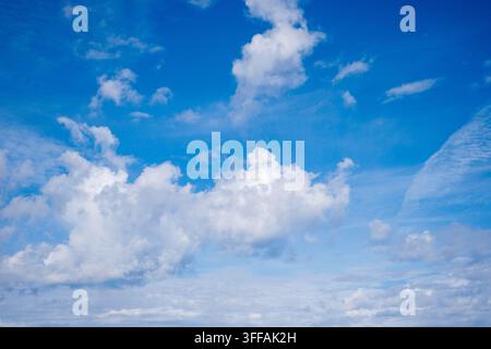 Des nuages cumulus imposants baignés de soleil et de plus petites formations nuageuses se détachent sur un ciel diurne intensément bleu. Banque D'Images