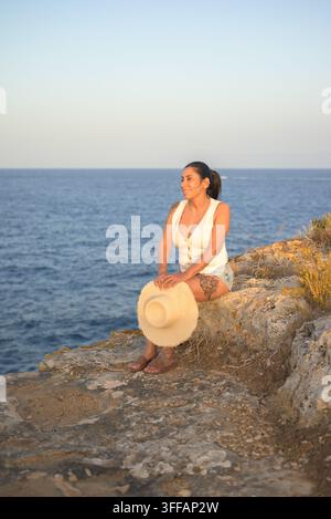 Femme se détendant sur une falaise rocheuse côtière au coucher du soleil Banque D'Images