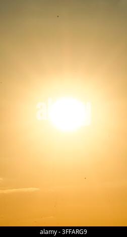 Un soleil intense de midi remplit le cadre d'un noyau blanc éblouissant et d'un dégradé ambré à travers le ciel, évoquant une chaleur brûlante, le minimalisme et la puissance brute de la lumière Banque D'Images