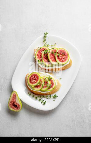 Toasts avec des figues fraîches, du fromage, du thym et du miel sur un fond clair. Concept d’une délicieuse entrée diététique de bruschetta et de fruits sur une assiette fo Banque D'Images