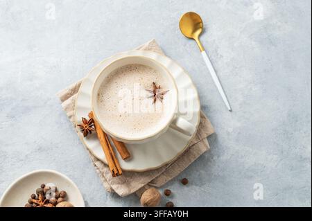 Thé masala chai indien traditionnel avec du lait et des épices dans une tasse blanche sur un fond bleu clair avec une cuillère. Un concept de boisson chaude confortable pour un menu ou b Banque D'Images
