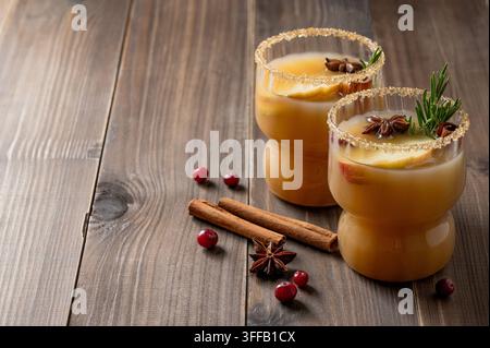 Deux verres de cidre de pomme chaud avec cannelle, anis, sucre brun et romarin sur un fond en bois avec canneberge. Concept une boisson traditionnelle et épicée Banque D'Images