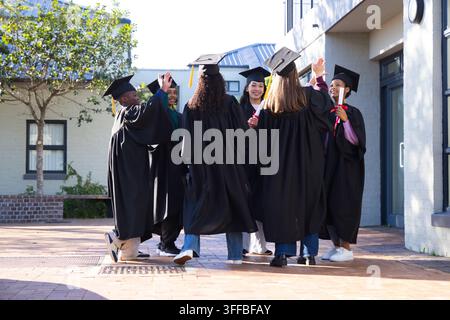 Différents étudiants portant des robes noires et des toges, célébrant dans la cour en tenant des tubes de diplôme rouges Banque D'Images