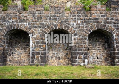 Une vue directe d'un vieux mur de pierre usé présentant trois alcôves ou niches arquées proéminentes. Le mur est construit en pierre gris foncé rugueuse a Banque D'Images