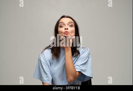 Jeune femme soufflant un baiser dans l'air, montrant de l'affection et envoyant de l'amour avec un geste ludique Banque D'Images
