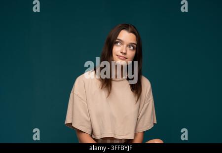 Jeune femme contemplant une idée en levant les yeux, pensant à ses projets futurs, posant sur un fond studio bleu-vert foncé Banque D'Images