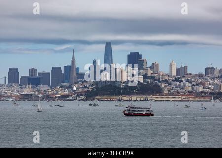 Un ferry navigue sur l'eau devant la skyline de San Francisco, avec des voiliers dispersés autour. Banque D'Images