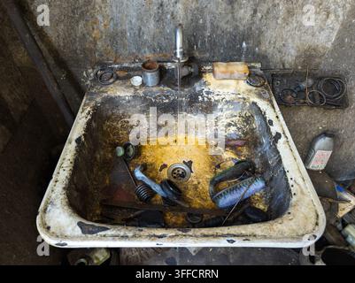 Vue aérienne d'un évier utilitaire sale rempli de crasse et de débris. L'eau coule d'un robinet chromé dans le bassin taché, entouré de murs en béton brut. Banque D'Images