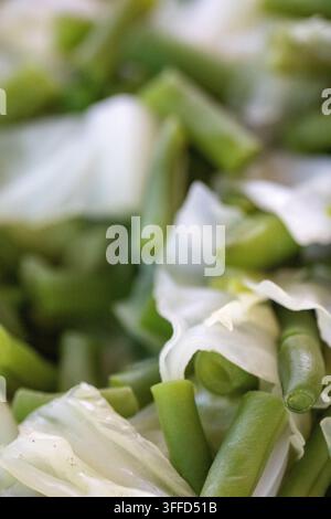 Une photo en gros plan verticale capturant un mélange culinaire frais de haricots verts coupés en dés et de feuilles de chou blanc croustillantes préparées pour la cuisson. Banque D'Images