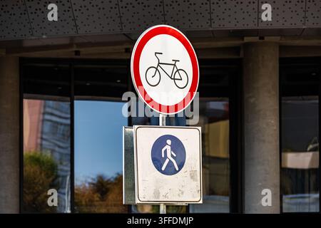 Panneau routier rond rouge interdisant le cyclisme empilé au-dessus d’un panneau rectangulaire bleu indiquant un chemin piéton sur un poteau métallique. Panneaux de régulation routière urbaine clairs installés n Banque D'Images