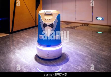Chengdu, Chine, Sichuan : 22 août 2025 : Serveur robot au design smoking debout sur un sol poli dans un restaurant contemporain, éclairé par sof Banque D'Images
