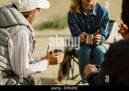 Groupe d'amis buvant du thé chaud dans des tasses pendant un voyage de camping Banque D'Images