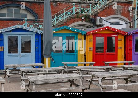 Cabanes de plage colorées et tables de pique-nique en bois vides dans une zone de café en plein air sur le front de mer à Brighton, en Angleterre. Banque D'Images