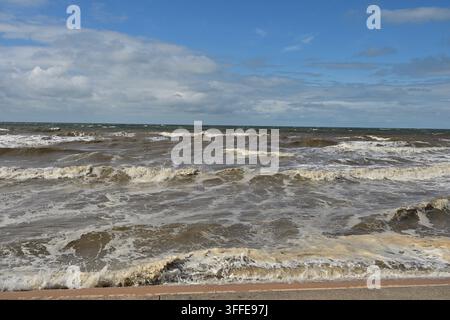 Paysage marin nuageux avec une eau brune agitée, une mousse blanche et un bord en béton en premier plan. Banque D'Images