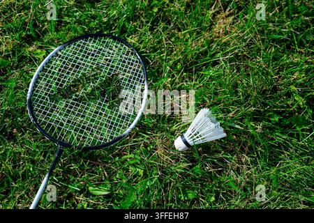 Composition minimaliste mettant en scène une raquette de badminton et un volant blanc posés sur de l'herbe verte vibrante en plein air Banque D'Images