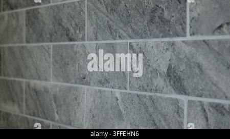 Des carreaux gris disposés selon un motif recouvrent un mur. La surface est lisse et uniforme. Le cadre suggère un design contemporain, probablement à l'intérieur. Banque D'Images