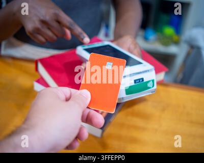 Un gros plan d'une main féminine tenant une carte de crédit ou de débit en plastique moderne contre un terminal de paiement sans contact (POS) blanc et élégant pour finaliser Banque D'Images