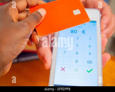 Un gros plan d'une main féminine non identifiable tenant une carte de crédit ou de débit en plastique moderne contre un terminal de paiement sans contact (POS) blanc et élégant Banque D'Images