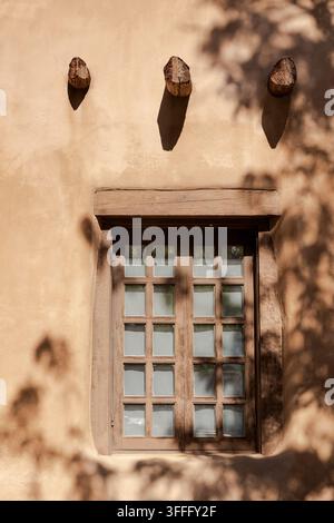 Fenêtre encadrée de bois sur des murs en adobe, Vigas et ombres fortes Banque D'Images