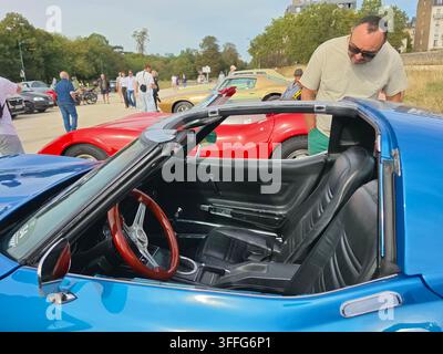 Homme inspectant l'intérieur d'une Chevrolet Corvette Stingray T-Top C3 bleue classique des années 1970 lors d'un salon de voitures anciennes en plein air, entouré de spectateurs Banque D'Images
