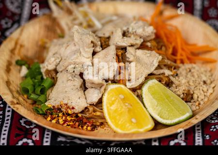 Poulet Pad Thai, un plat thaïlandais populaire de nouilles de riz sautées, garni de poulet tranché, de citron vert, de cacahuètes écrasées et d'oignons de printemps Banque D'Images
