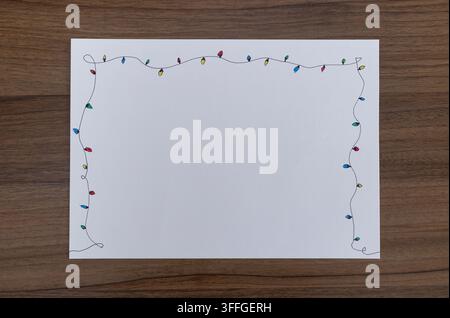 Papier texturé vierge avec une bordure de guirlandes colorées dessinées à la main sur une table en bois sombre, vue de dessus, prêt pour une note de fête Banque D'Images