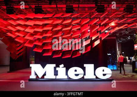 Berlin, Allemagne, 8 septembre 2026. Un grand logo blanc illuminé du fabricant allemand d’électroménager haut de gamme Miele se dresse au stand de l’entreprise lors de l’IFA 2026 (Innovation For All) à Berlin. Au-dessus de l’inscription de marque proéminente se trouve une installation artistique en forme de vague composée de nombreux panneaux rectangulaires rouges qui se chevauchent, créant un auvent architectural dynamique illuminé sous un éclairage studio rouge intense. En arrière-plan de la salle d’exposition, des visiteurs de salon passent devant des écrans d’affichage et des zones de présentation de produits. Crédit : Felix Wolf/Alamy Live N Banque D'Images