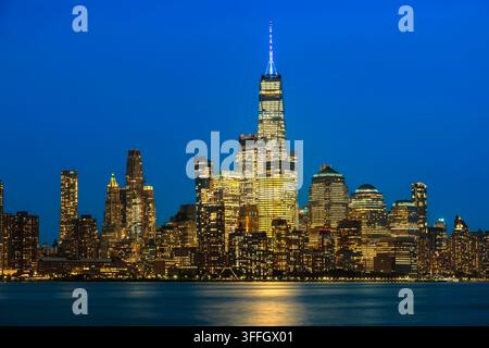 Une vue illuminée du centre-ville de Manhattan brillant au crépuscule avec les lumières de la ville se reflétant sur le fleuve Hudson à New York City. Banque D'Images
