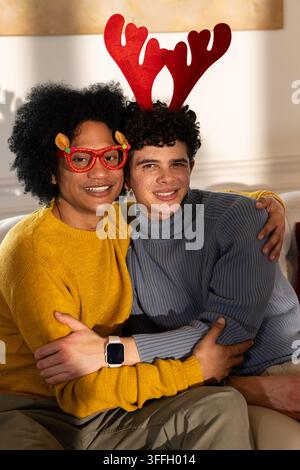 Partenaires masculins africains assis sur le canapé de la maison portant des lunettes rouges pailletées et un bandeau en bois de renne Banque D'Images