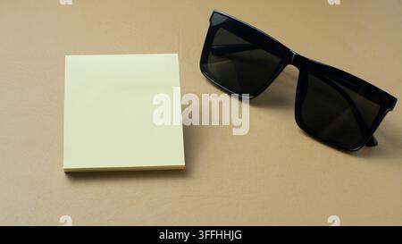 Post-it vierge et lunettes de soleil sur fond beige, adapté pour la planification du style de vie, le rappel de voyage, l'accessoire de mode Banque D'Images