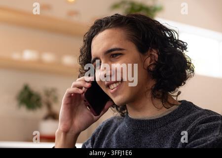 Homme afro-américain souriant tout en tenant un smartphone avec une coque sombre à la maison dans un pull en tricot sombre Banque D'Images