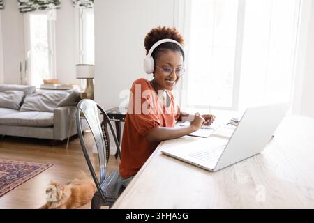 Jeune femme africaine portant des écouteurs, prenant des notes pendant un cours en ligne Banque D'Images
