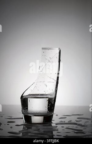 un verre brisé rempli d'eau avec de nombreux éclaboussures et gouttelettes sur la surface et la table en contre-jour Banque D'Images