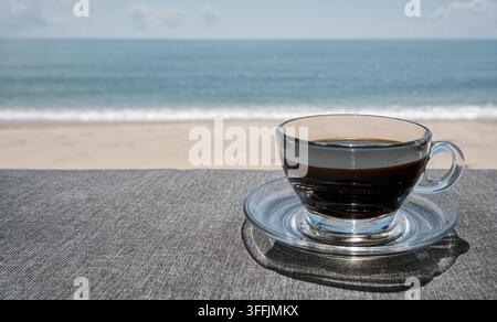 tasse transparente de café noir sur la table devant la plage et la mer ouverte Banque D'Images