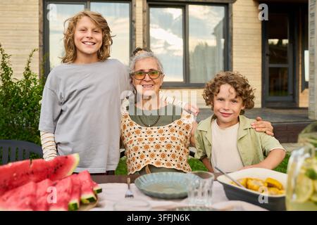 Portrait d'une femme âgée souriant avec ses petits-enfants à une table dans le jardin Banque D'Images