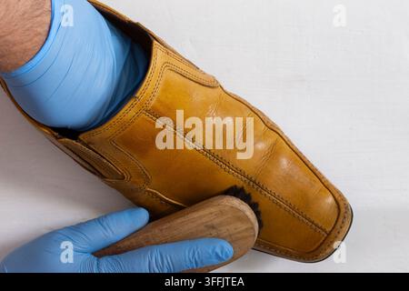 Polissage d’une chaussure en cuir marron à enfiler avec une brosse à chaussures. Sur un fond en bois blanc. Banque D'Images