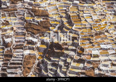 Vue de la saline de Maras présentant des étangs d'évaporation en terrasses complexes avec des nuances variées de blanc et de brun de la terre à Urubamba, Cusco, Pérou. Banque D'Images