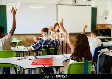 Élèves d'école primaire levant la main, montrant leur enthousiasme et leur engagement pendant une leçon avec leur enseignant dans la salle de classe Banque D'Images