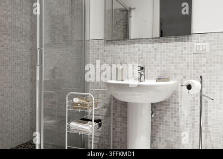 Processus de rénovation de salle de bain avec nouvelle mosaïque de carreaux en céramique murale. Rénovation moderne de toilettes montrant un lavabo sur pied blanc et une cabine de douche en verre Banque D'Images