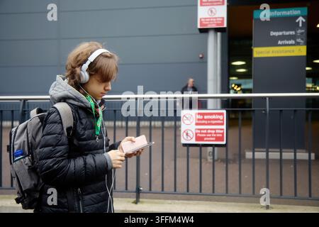 Jeune voyageur utilisant un smartphone et un casque à l'aéroport Banque D'Images