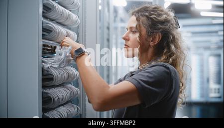 Technicienne IT féminine effectuant le câblage RJ45 à l'intérieur d'un rack de serveur, routant les câbles réseau à travers les gestionnaires de câbles et vérifiant les connexions physiques pour la maintenance et le service du câblage structuré. Banque D'Images
