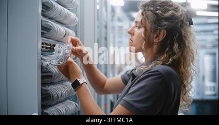 Technicienne IT féminine effectuant le câblage RJ45 à l'intérieur d'un rack de serveur, routant les câbles réseau à travers les gestionnaires de câbles et vérifiant les connexions physiques pour la maintenance et le service du câblage structuré. Banque D'Images