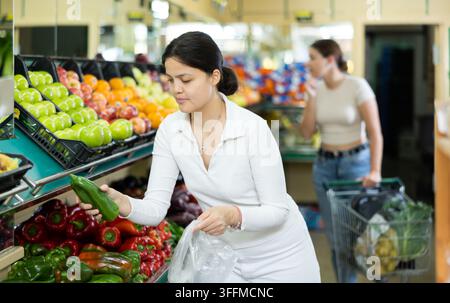 Jeune femme acheteuse en vêtements décontractés choisit des poivrons dans le supermarché Banque D'Images
